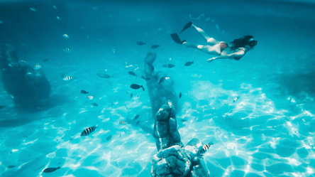 Cancun Sailing Catamaran above Cancun Ocean statues of fingers and a girl snorkeling underwater